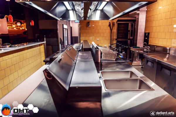 The kitchen line under the custom exhaust canopy, with the pass and prep bench