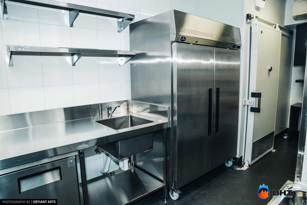 Two-door upright fridge beside the cool room door, with a stainless sink bench along the wall
