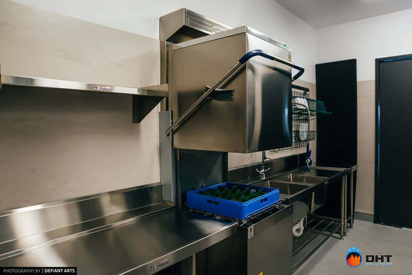 Electrolux pass-through dishwasher with its hood raised, flanked by stainless inlet and outlet benches
