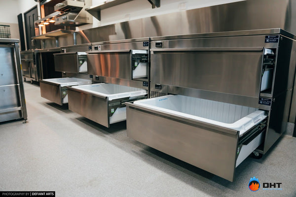 A run of Adande refrigerated drawers pulled open along the kitchen wall beneath the pass