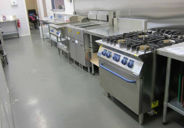 The back-of-house cooking line with fryers, gas oven range and dishwasher