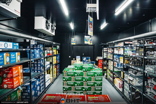 Inside the walk-in cool room, with beer cartons stacked between shelving and ceiling evaporators overhead