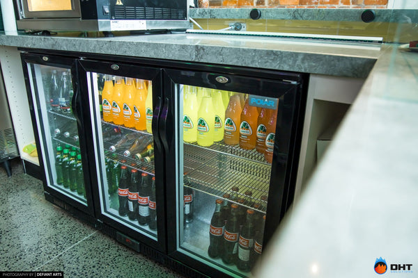 Three glass-door under-counter fridges stocked with soft drinks beneath the servery