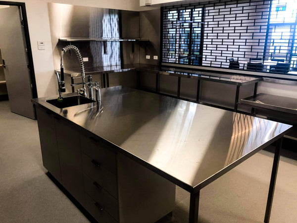 Custom stainless island bench with a sink and pre-rinse tap, beside the servery window to the function room